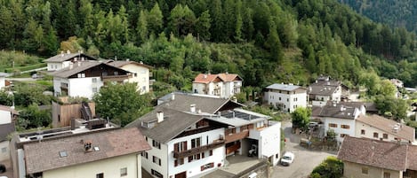 A residential area with houses featuring sloped roofs and balconies, surrounded by dense forest.