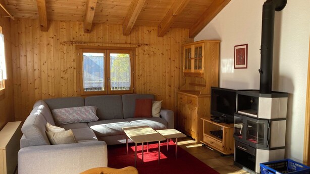 En hyggelig stue med trælofter, en grå sofa, en rød måtte og en sort pejs.
