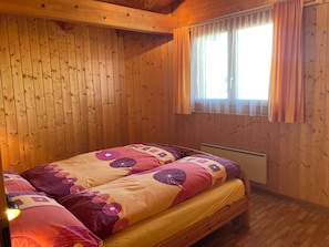 Quarto de cabana de madeira com cama, janela com cortinas e radiador.