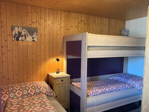 Ett rum med en våningssäng, ett sängbord med en lampa, mönstrat sänglinne och en tavla som hänger på väggen.