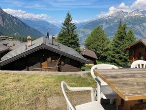 A mountain lodge with a wooden exterior, a dining area with a table and chairs, and a view of snow-capped mountains.