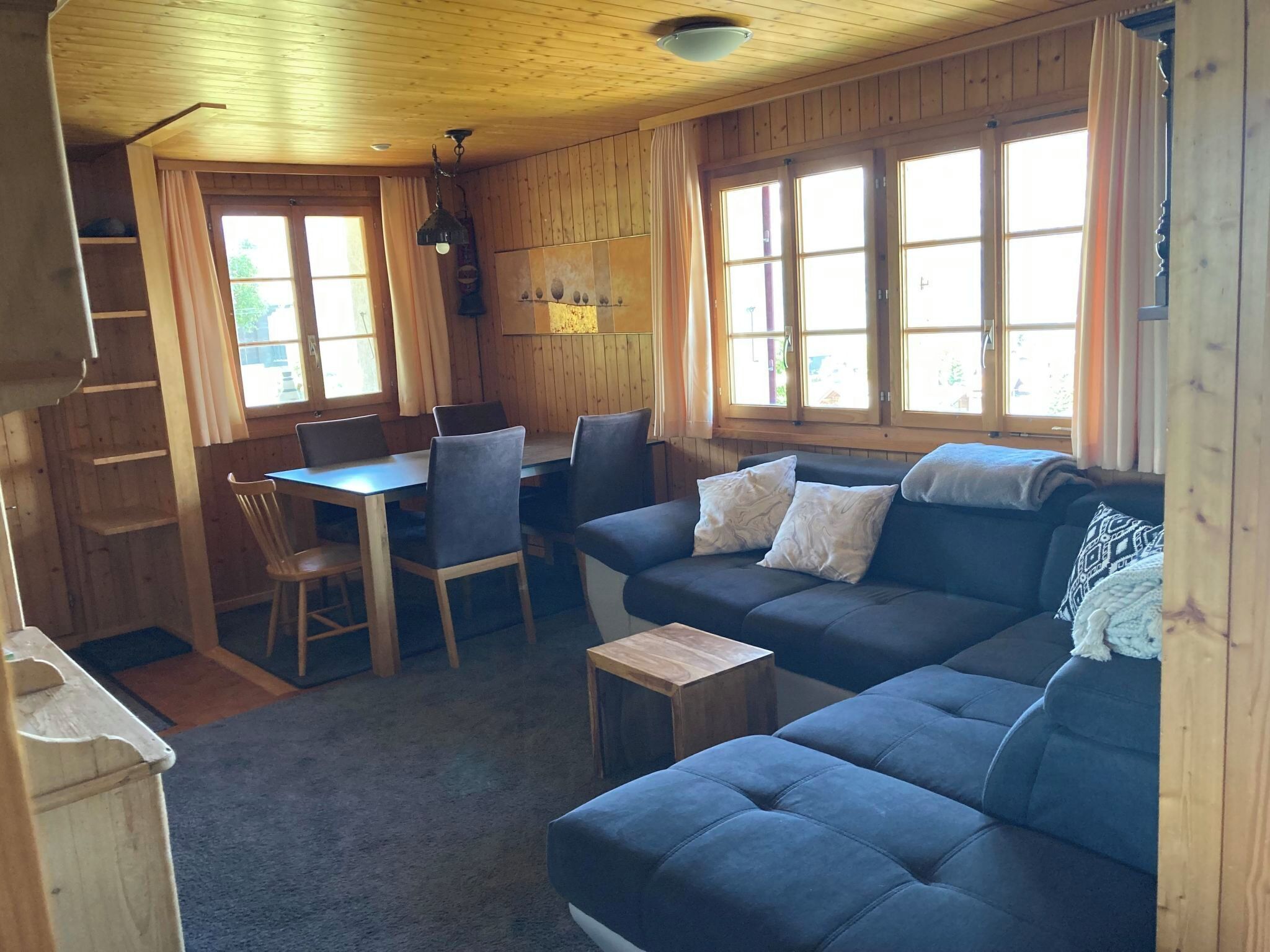 Um quarto aconchegante com um sofá azul, uma mesa de jantar com cadeiras e janelas amplas.