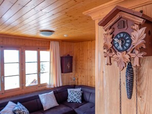 A wooden interior with a large cuckoo clock, a sofa, and a window with curtains.