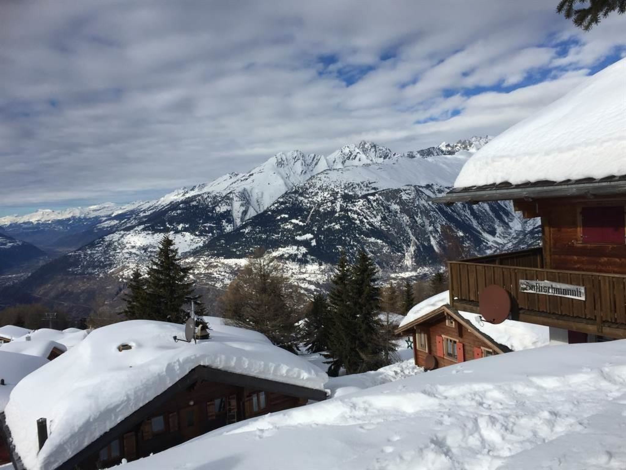 A mountain lodge with snow-covered roofs and a view of snow-capped mountains.