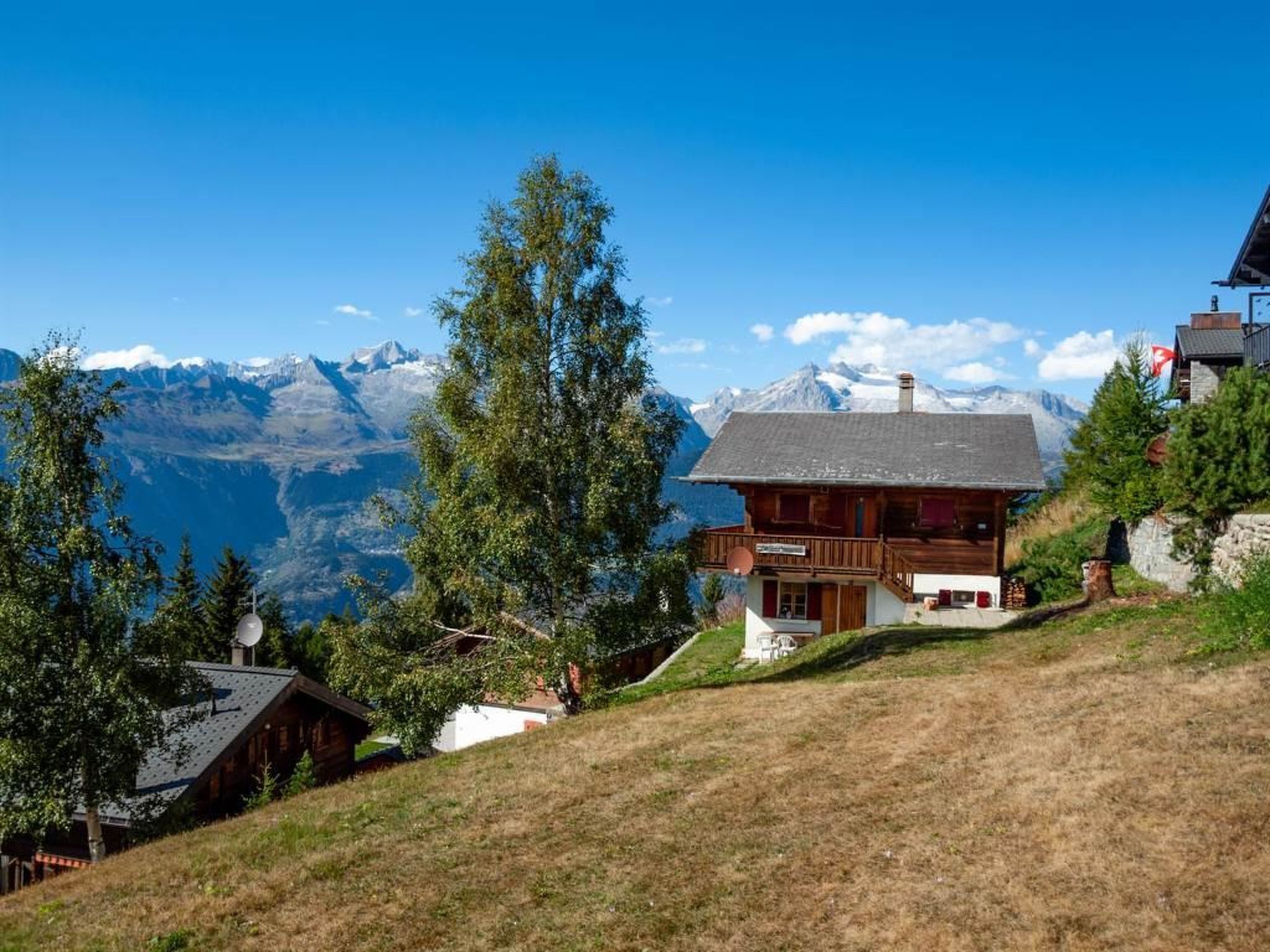 Een houten chalet met balkon, omringd door bomen en een berg op de achtergrond.