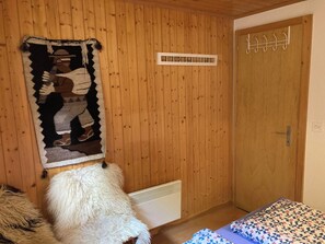Ett rum med träväggar, en säng med ett mönstrat överkast, en upphängd väv och en klädställning.