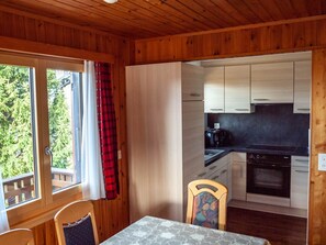 Ein Holzblockhaus-Interieur mit Essbereich, Küche und einem Fenster mit Vorhängen.