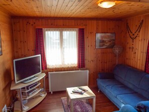 A cozy living room with a television on a stand, a blue sofa, a small table with books, and a radiator.