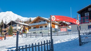 A ski resort with a wooden fence, a red sign, and buildings with snow-covered roofs. - Chalet Valeria 4-Bettwohnung, Parterre, 2 Schlafräume Valeria EG by Interhome (Rosswald)