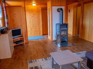 Interior acolhedor de uma cabana com piso de madeira, uma televisão sobre um suporte, uma lareira e uma pequena mesa.