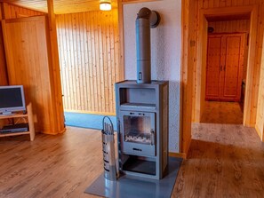 A room with a wood-burning stove, a television on a stand, and wooden walls. - Chalet Valeria 4-Bettwohnung, Parterre, 2 Schlafräume Valeria EG by Interhome (Rosswald)
