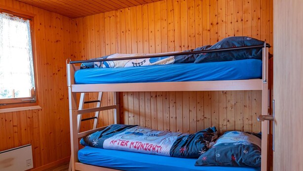 A bunk bed room with wooden walls and a window. - Chalet Valeria 4-Bettwohnung, Parterre, 2 Schlafräume Valeria EG by Interhome (Rosswald)