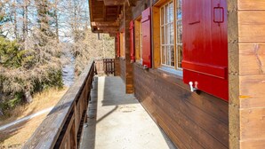 A wooden cabin with a covered porch, red shutters, and a view of the surrounding forest. - Chalet Valeria 4-Bettwohnung, Parterre, 2 Schlafräume Valeria EG by Interhome (Rosswald)