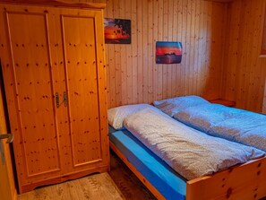 Quarto de madeira com uma cama beliche, um guarda-roupa e duas imagens penduradas na parede.