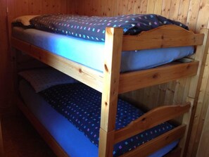 Ein Etagenbett mit drei Schlafstellen, jede mit einem Kissen und einer blauen Decke mit Muster.