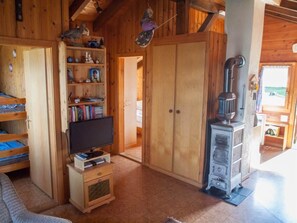 A wooden interior with a television on a wooden stand, a bookshelf, a wardrobe, and a wood stove. - Chalet Alphütte Appartement/Fewo, Dusche, WC 4-Bettwohnung Dachgeschoss by Interhome (Rosswald)
