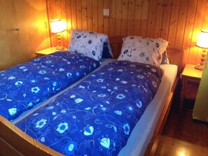 Una cama doble con ropa de cama estampada con motivos florales, dos lámparas de noche y paredes de madera.