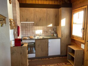 A compact kitchen with wooden cabinets, a stove, a sink, and a refrigerator. - Chalet Alphütte Appartement/Fewo, Dusche, WC 4-Bettwohnung Dachgeschoss by Interhome (Rosswald)