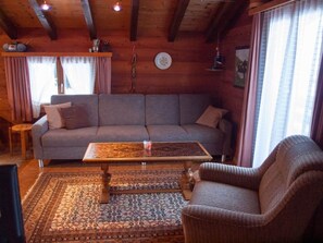 A cozy living room with a sofa, a patterned rug, a wooden coffee table, and a wicker armchair. - Chalet Alphütte Appartement/Fewo, Dusche, WC 4-Bettwohnung Dachgeschoss by Interhome (Rosswald)
