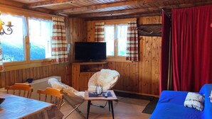 Interior acogedor de una cabaña con techo de madera, televisor, mesa de comedor y sofá.
