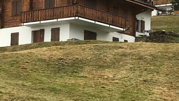 Una casa de madera de dos pisos con un balcón, frente a un paisaje montañoso.