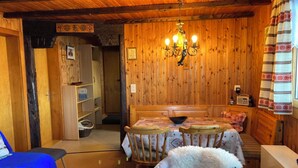 Una habitación acogedora con paredes de madera, un candelabro, una mesa de comedor con sillas, un sofá azul y un sillón blanco mullido.
