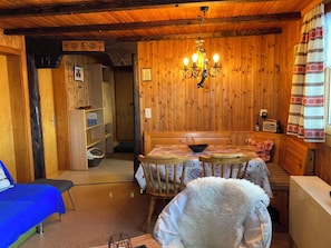 Ein gemütlicher Raum mit Holzwänden, einer Kristallleuchtre, einem Esstisch mit Stühlen, einem blauen Sofa und einem flauschigen weißen Sessel.