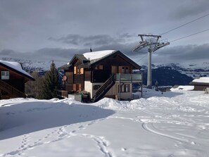 Un chalet en bois, avec un télésiège visible en arrière-plan, entouré de montagnes enneigées.