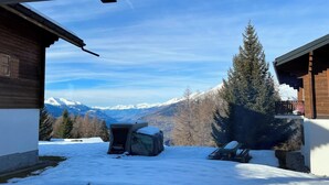 Eine verschneite Landschaft mit einer Holzhütte und freiem Blick auf schneebedeckte Berge.