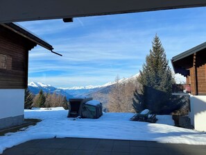 Eine verschneite Landschaft mit einer Holzhütte und freiem Blick auf schneebedeckte Berge.
