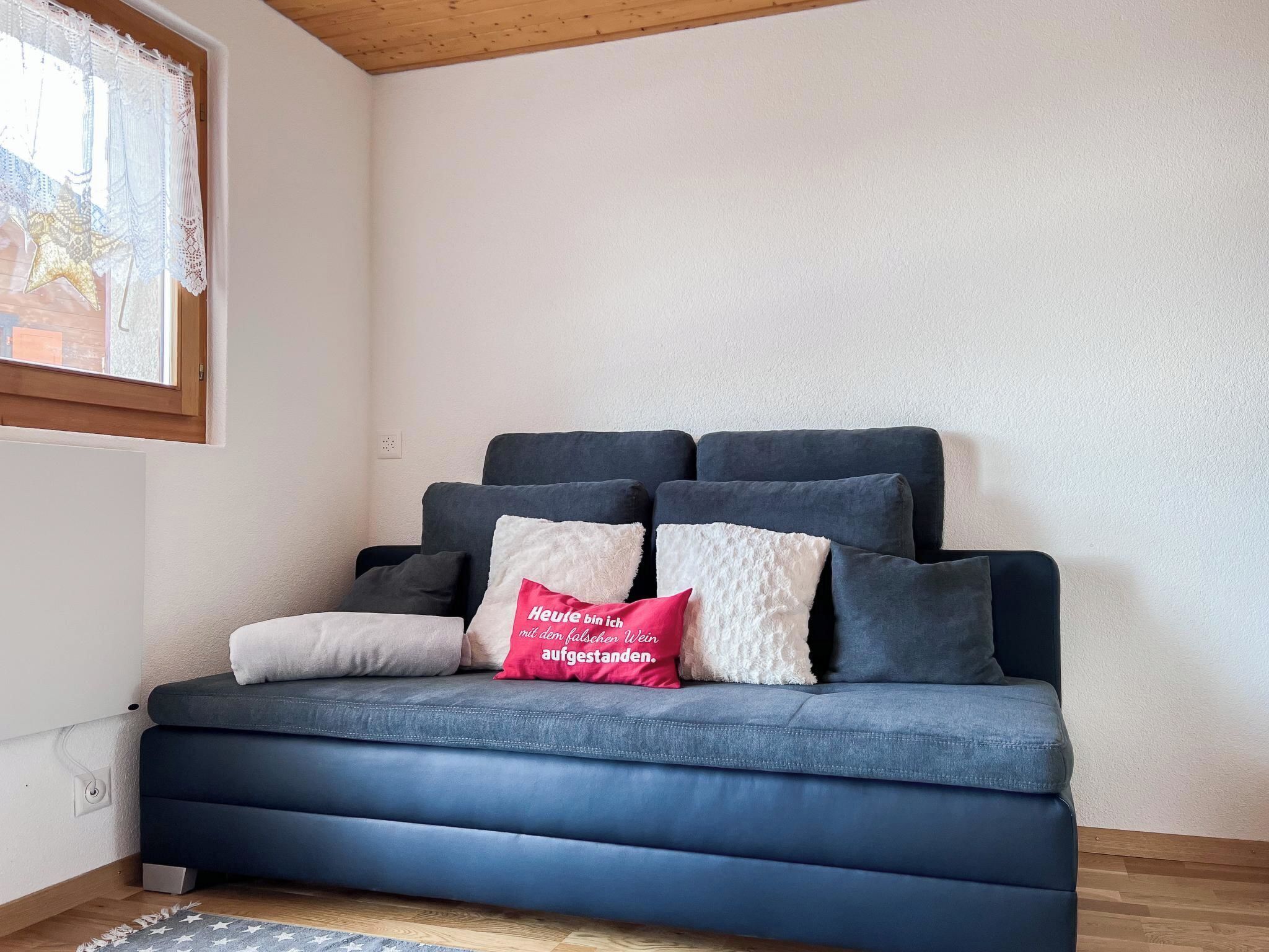 Ein dunkelblaues Sofa mit vielen Kissen, ein rotes Kopfkissen mit Schriftzug und eine Stern-Dekoration am Fenster.