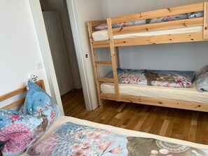 Ein Etagenbett mit floralem Bettzeug, Holzboden und eine Tür zu einem anderen Zimmer.