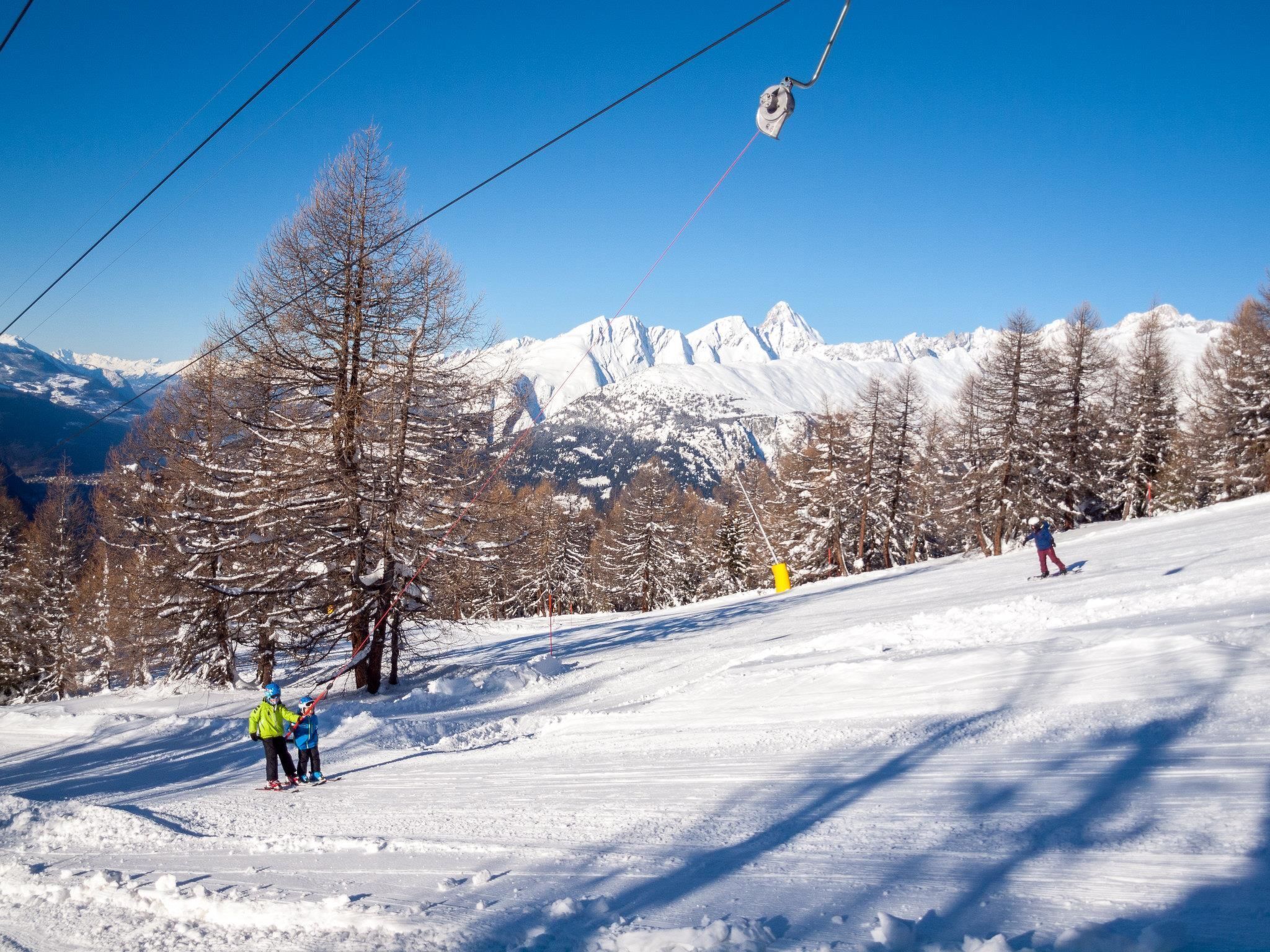 Pista de esqui com esquiadores, um teleférico e árvores cobertas de neve.