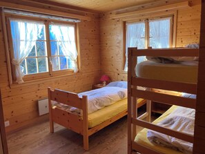 Une chambre rustique en bois, avec des lits superposés, une petite table de chevet et deux fenêtres équipées de rideaux.
