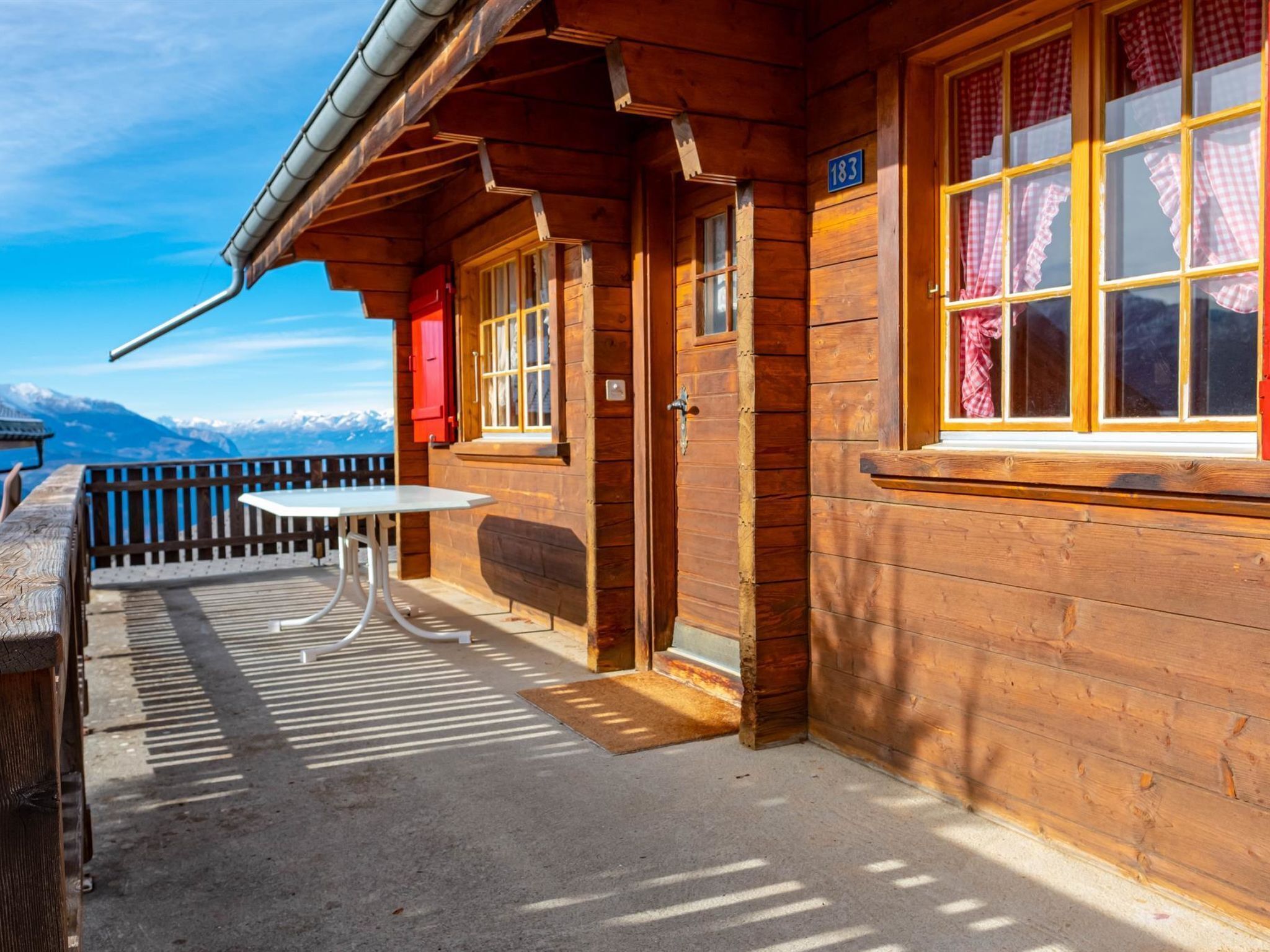 Une cabane en bois dotée d’un balcon, d’une table et offrant une vue sur les montagnes.
