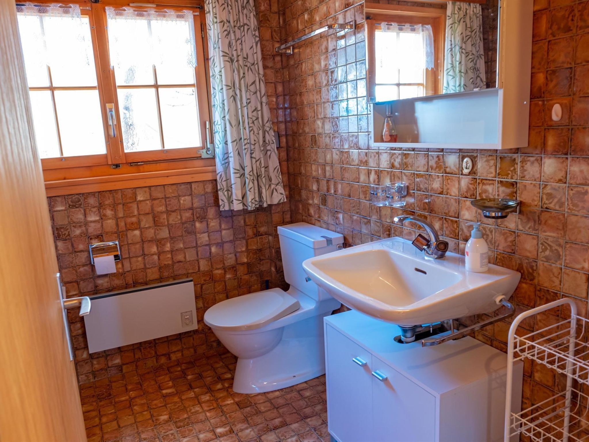 Baño con inodoro, lavamanos y ventana con cortinas.