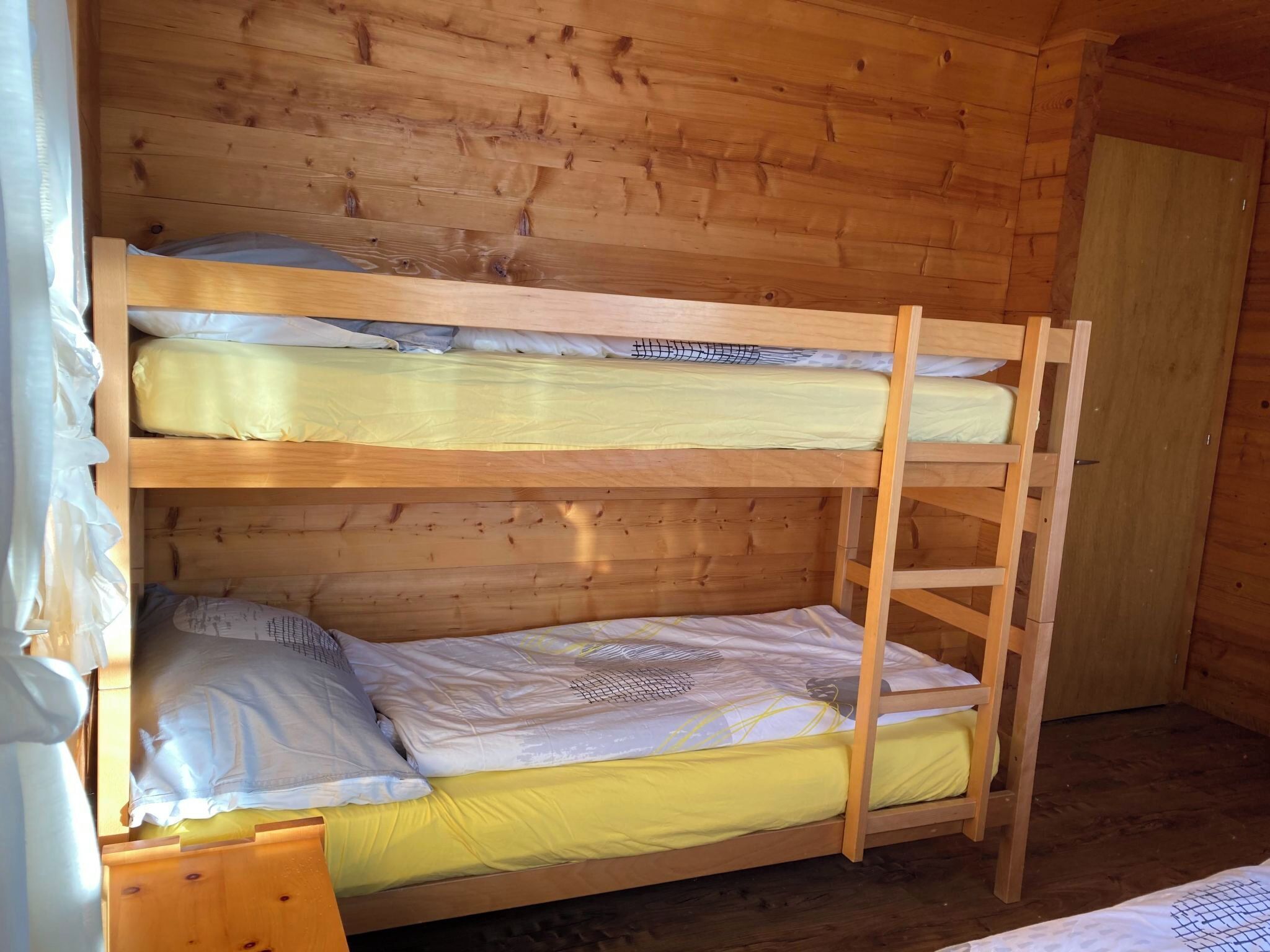 A bunk bed with two levels, wooden walls, and a door.