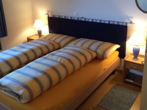Een bed met gestreepte lakens, twee bedlampjes en een klein nachtkastje met een lamp.