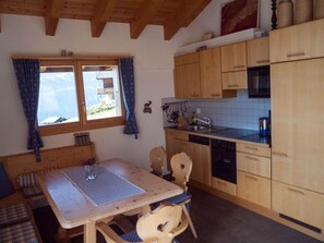 A cozy kitchen with wooden cabinets, a dining table, and a view of the outdoors through a window. - Chalet Bergkristall 4-Bettwohnung, Dusche, WC 4-Bettwohnung, Dusche, WC by Interhome (Rosswald)