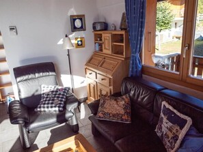 Een woonkamer met een lederen fauteuil, een bank, een houten kast en een raam met uitzicht op de omgeving.