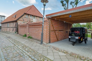 A brick building with a red-tiled roof, a covered parking area, and a parked three-wheeled vehicle.