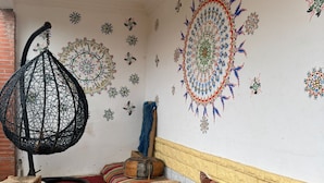 Una habitación con techo bajo, un sillón colgante, una mesa redonda azul, un sofá estampado y decoración en la pared.