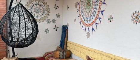 A room with a low ceiling, a hanging chair, a blue round table, a patterned sofa, and decorative wall art.