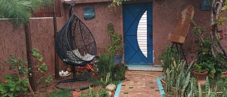 Un chemin de jardin bordé de bleu, une chaise suspendue et une porte bleue.