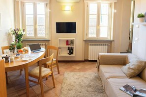 A cozy living room with a sofa, a dining table with chairs, a TV, and a shelf with books and a plant. - Apartment in Lucca with private furnished terrace (Lucca)