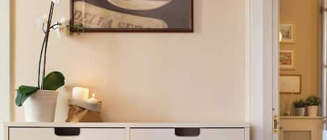 A white cabinet with two drawers and a small shelf, a framed picture of a cup of coffee, and a white orchid on the shelf.