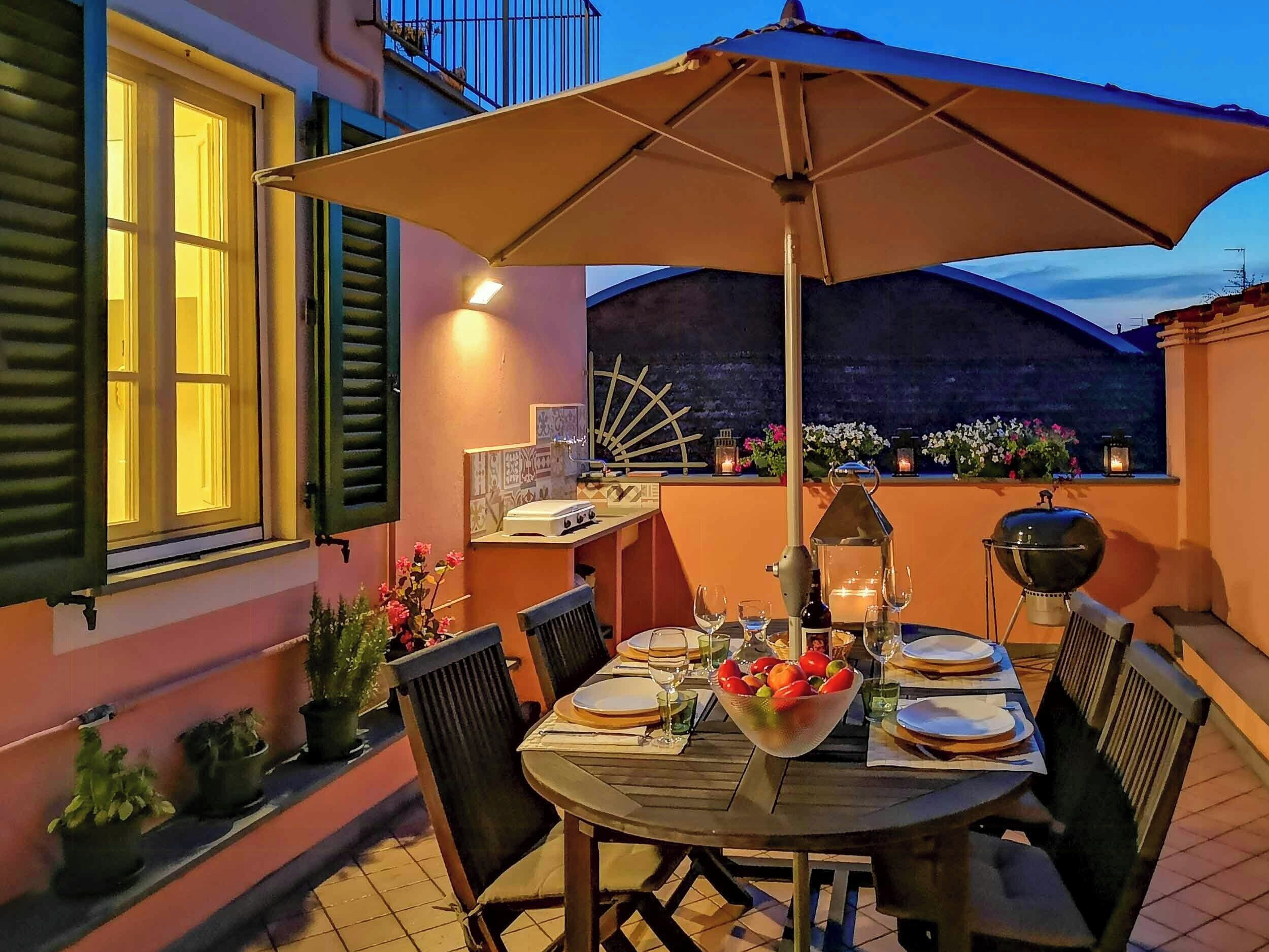Un espace de restauration en plein air avec une table dressée pour quatre personnes, entourée de chaises, et protégée par un grand parasol.