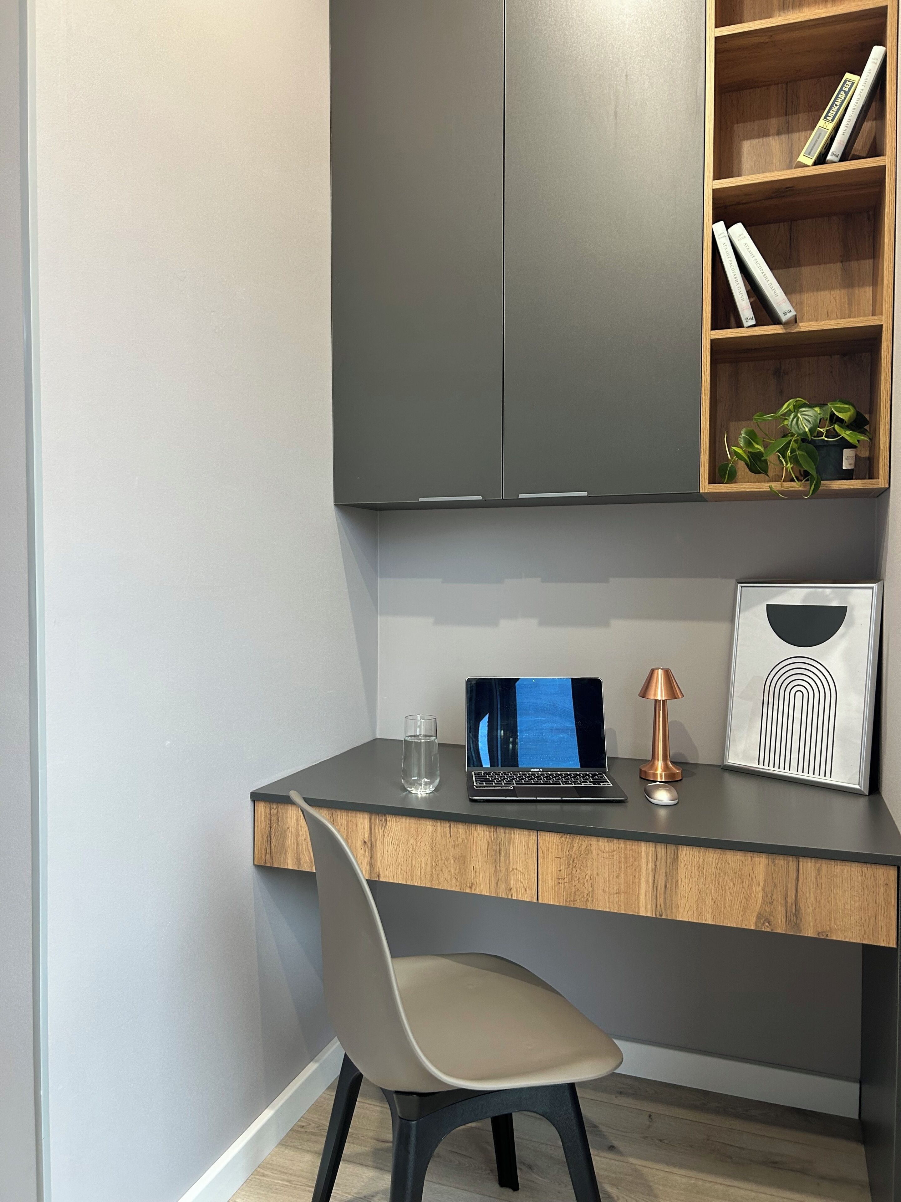 A modern workspace with a grey desk, a laptop, a glass of water, a lamp, and a framed picture.