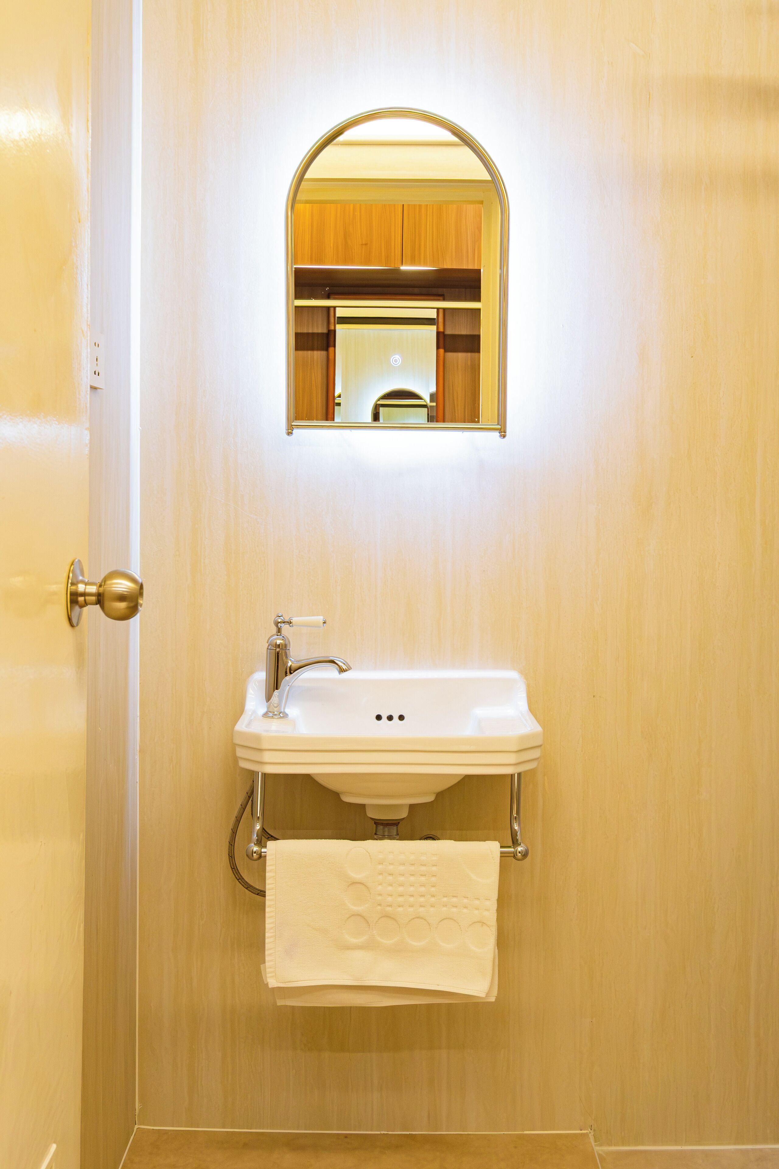 Un baño con puerta de madera, un lavamanos con toalla y un espejo.