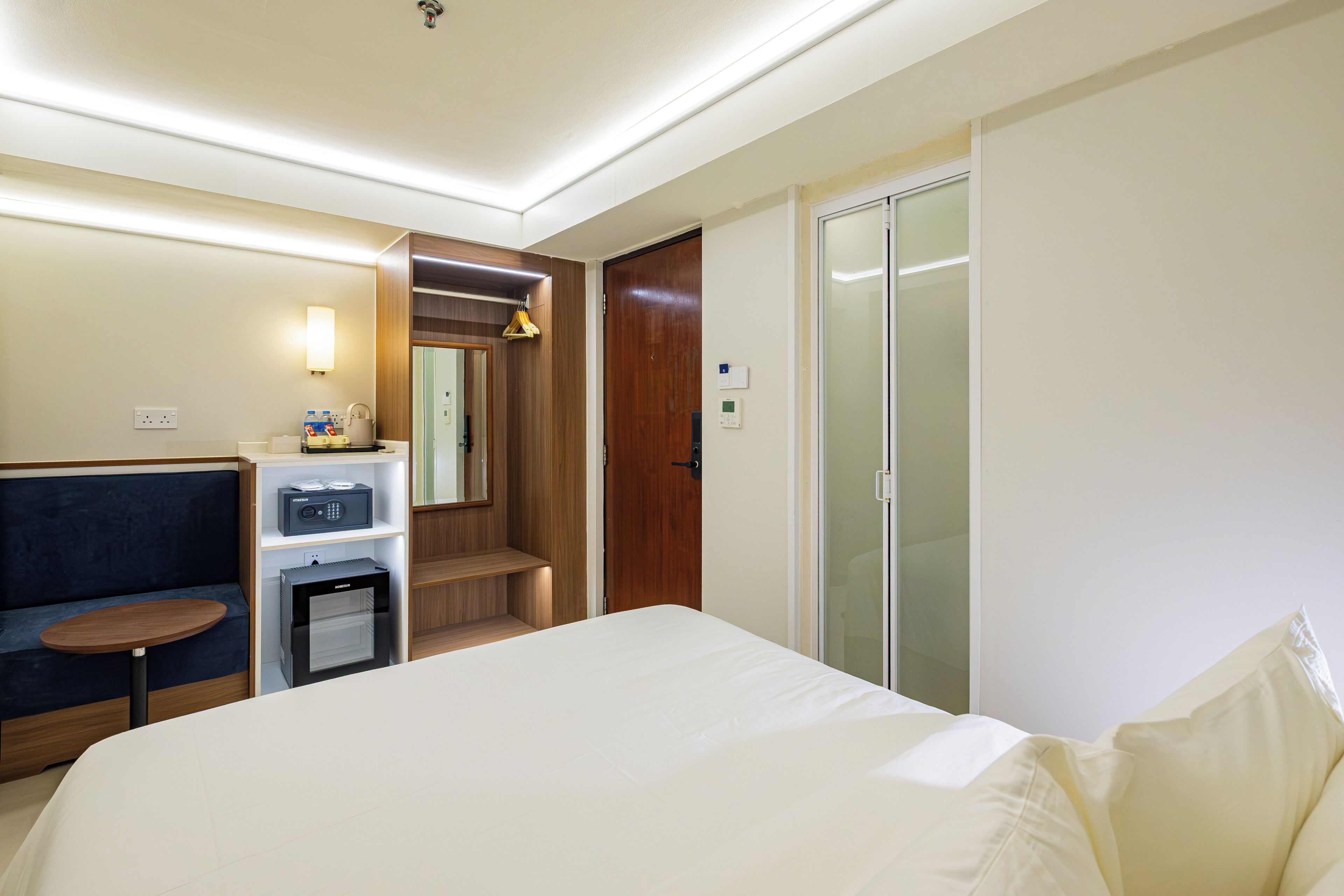 A hotel room with a bed, a seating area, a minibar, a coat rack, and a wardrobe.